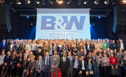 large group of employees with SPIG logo on screen in background