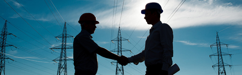 construction workers shaking hands with electricity towers in background