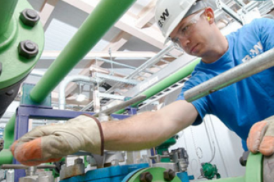 A man in a hardhat, safety glass and protective gloves working in an industrial facility