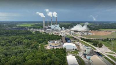 Aerial view of a coal-fired power plant puffing steam into the sky, surrounded by woodlands