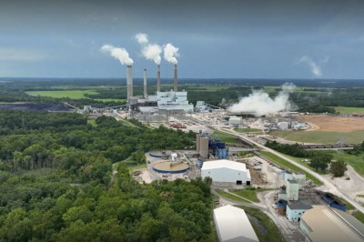 Aerial view of a coal-fired power plant puffing steam into the sky, surrounded by woodlands