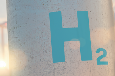Close up view of a hydrogen storage tank with a wind turbine in the background