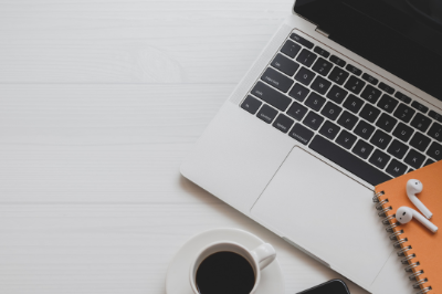 Laptop computer, coffee cup, earbuds and a paper notepad on a table