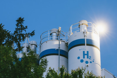 Large hydrogen storage tanks against a sunny sky with trees in the foreground
