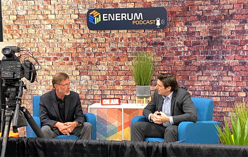 Two men sitting on chairs in front of a brick wall having an on-camera discussion