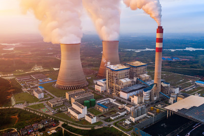 aerial view of a power plant with steam coming out of the cooling towers and stacks