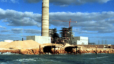 gas power plant construction with cloudy sky and shore in foreground