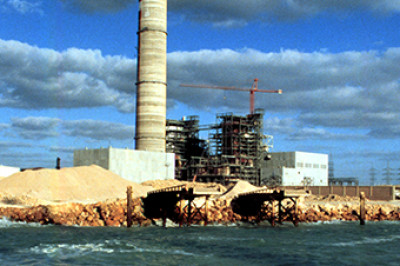 gas power plant construction with cloudy sky and shore in foreground