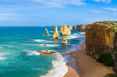 stock image of the Australian coastline depicting waves on a beach and large rock cliffs jutting from the water and shoreline