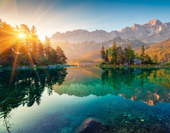 sun rising over lake with mountains in background